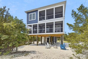 A two-story beachfront house with a covered patio and outdoor seating.