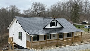 A two-story house with a porch, a metal roof, and a wooden deck. - New Cabin built in 2022. 2 minutes away from multiple trailheads!  Sleeps 8 (Rock)