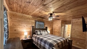 A wooden-paneled bedroom with a bed, nightstands, a ceiling fan, and a window with curtains. - New Cabin built in 2022. 2 minutes away from multiple trailheads!  Sleeps 8 (Rock)