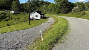 A rural road with a gravel shoulder and a white house with a dark roof. - New Cabin built in 2022. 2 minutes away from multiple trailheads!  Sleeps 8 (Rock)