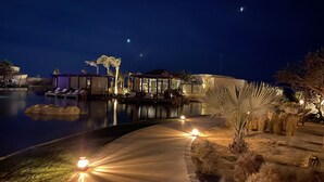 Une vue nocturne d’un complexe hôtelier avec une piscine, des chaises longues et un chemin bien éclairé.