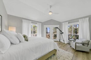 Ein Schlafzimmer mit einem großen Bett, einem Schreibtisch und einem Stuhl, mit Blick ins Freie durch eine Tür.
