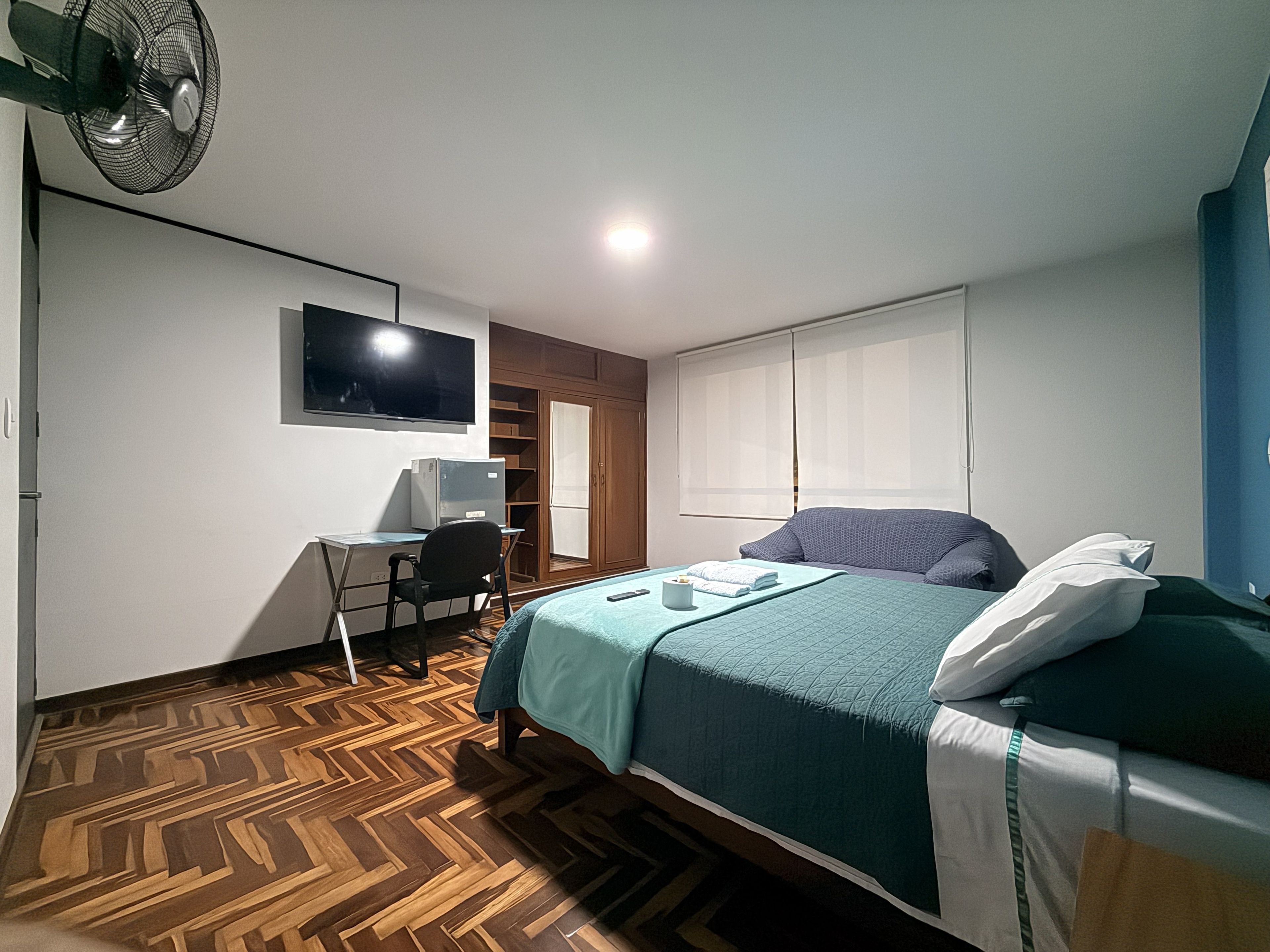 Un dormitorio con cama, escritorio, silla, televisión y armario.