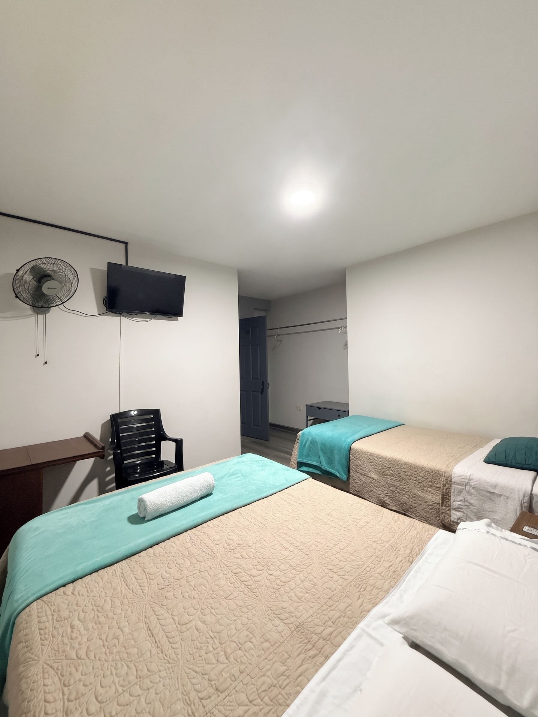A hotel room with two beds, a chair, a TV, and a fan.