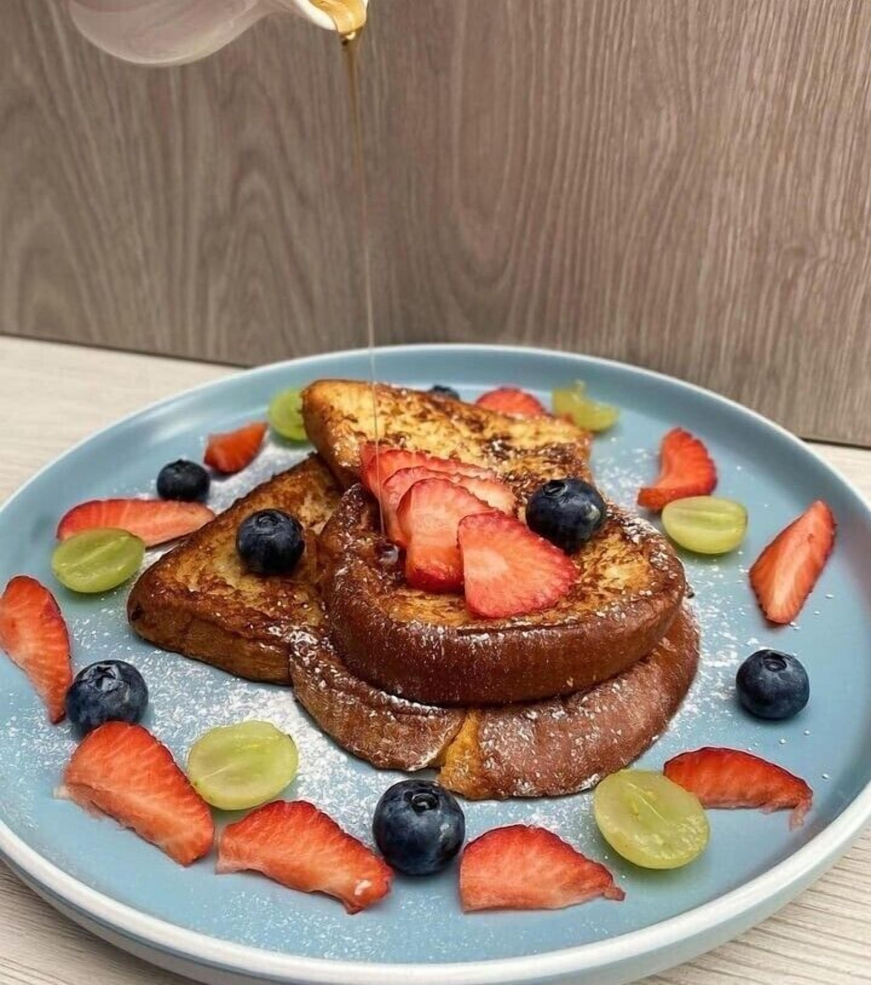 Un plato de panes fritos con fresas y arándanos, servido en un plato azul.
