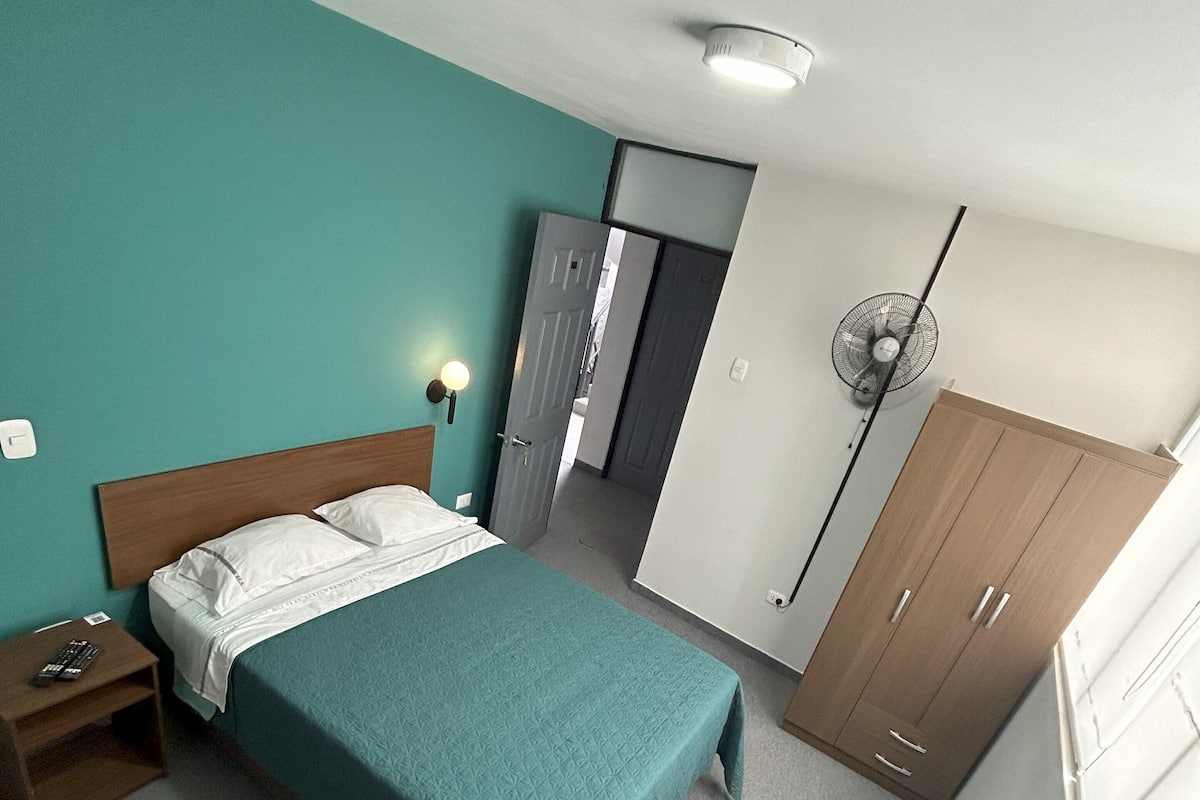 A bedroom with a bed, nightstand, wardrobe, and a ceiling fan.
