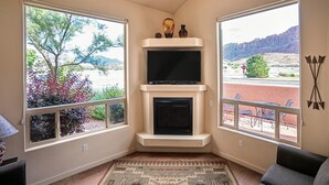 Habitación de esquina con chimenea, televisión y ventanas amplias con vistas a un paisaje desértico.