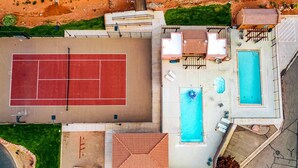 Vista aérea de una propiedad residencial con cancha de tenis, dos piscinas y zonas de estar al aire libre.