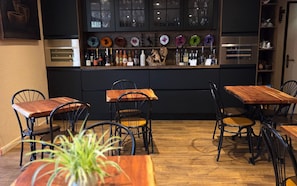 A bar area with wooden tables and chairs, a shelf with bottles, and a decorative wall with plates. - Hôtel L'Etoile - Airport - A61 (Carcassonne)