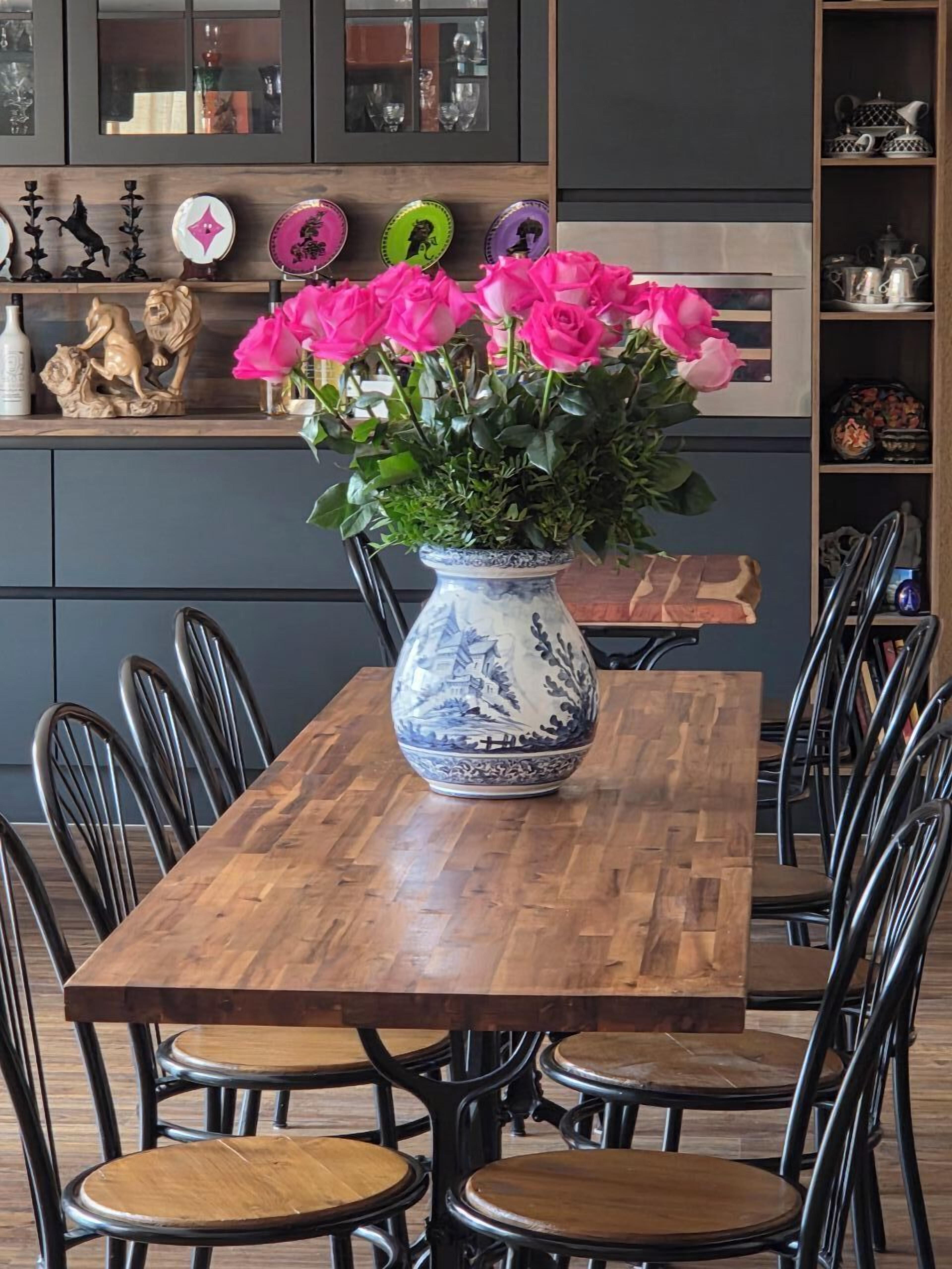 Una mesa de comedor con un jarrón de flores rosadas, rodeada de sillas negras.