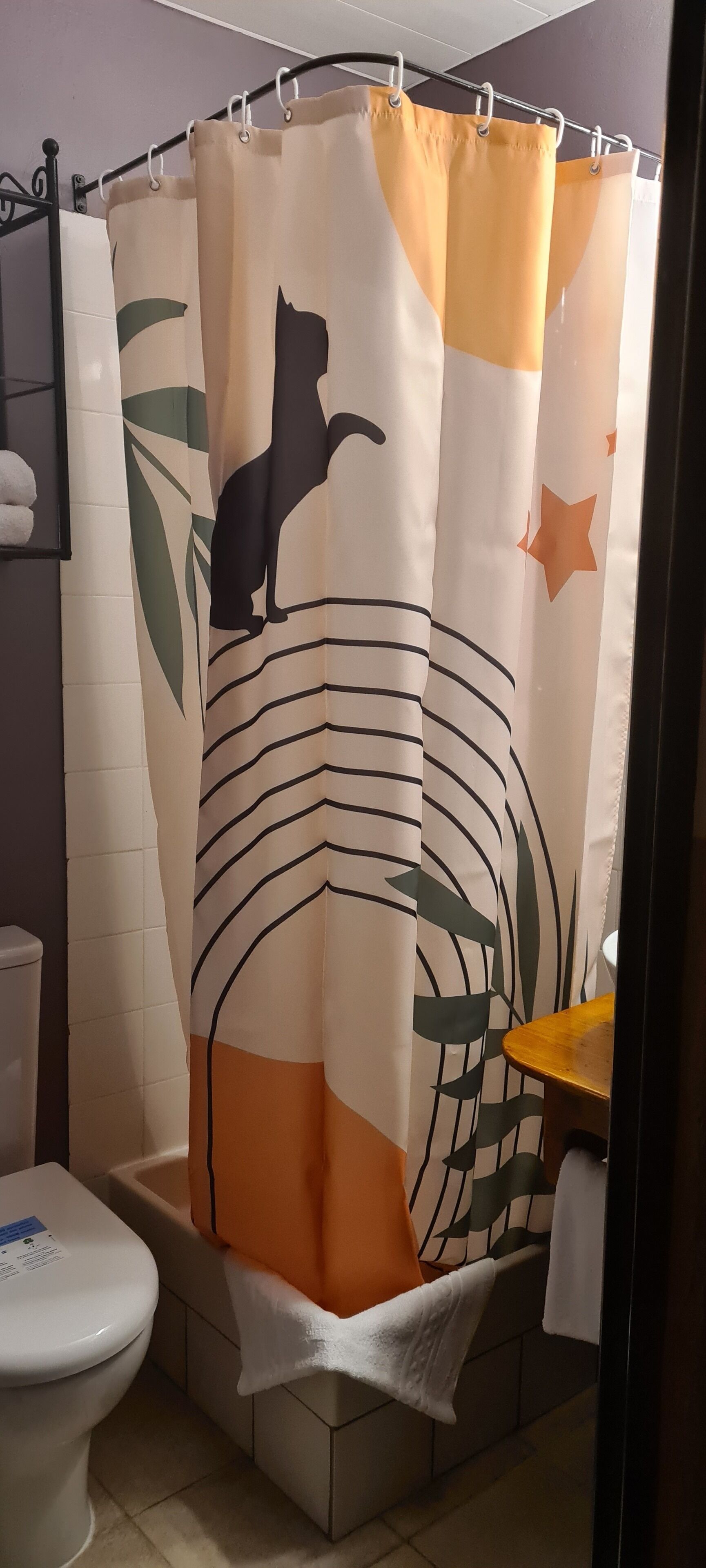 Un baño con cortina de ducha con silueta de gato, un inodoro y un lavabo con una toalla.