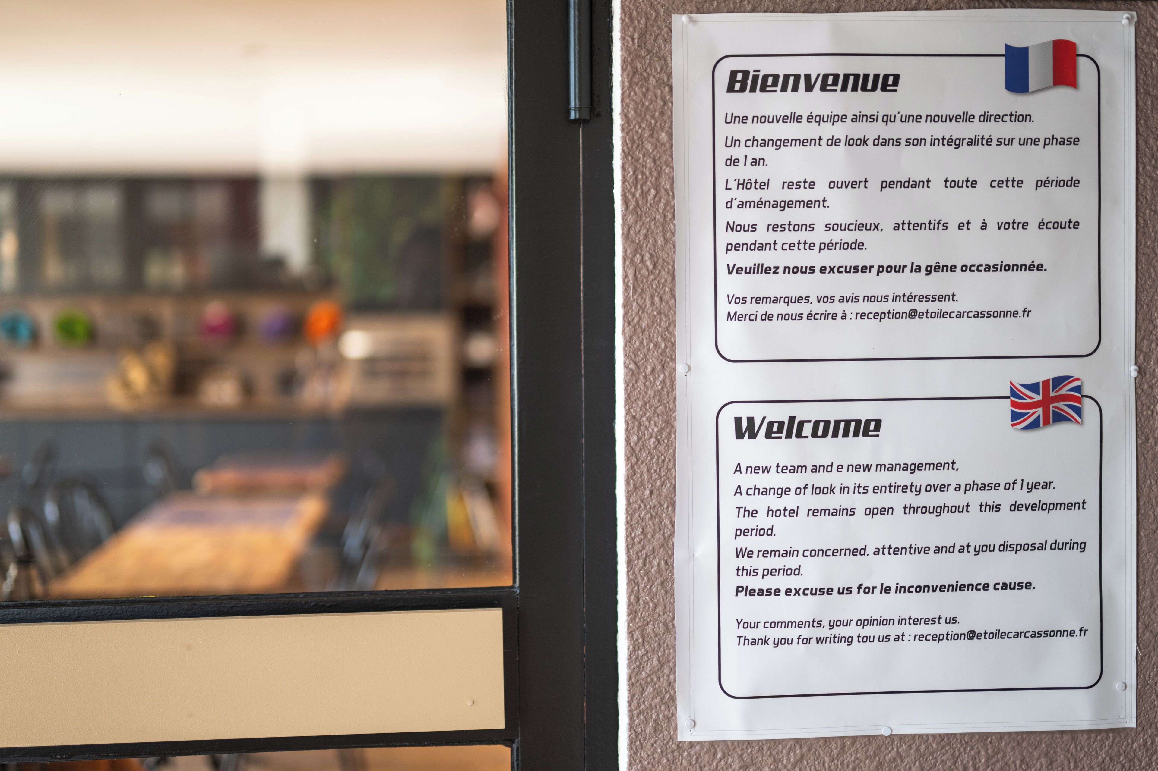 En välkomstskylt med text på franska och engelska, en flagga och en e-postadress för receptionen.