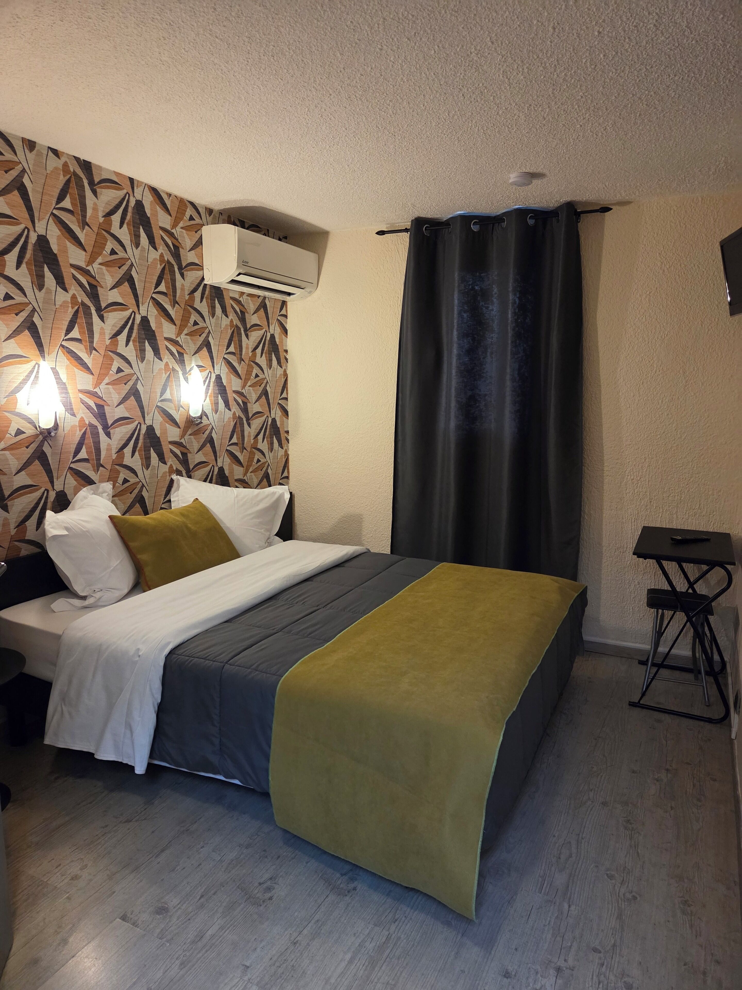 Un dormitorio con cama, mesita de noche, aire acondicionado de pared y cortina.