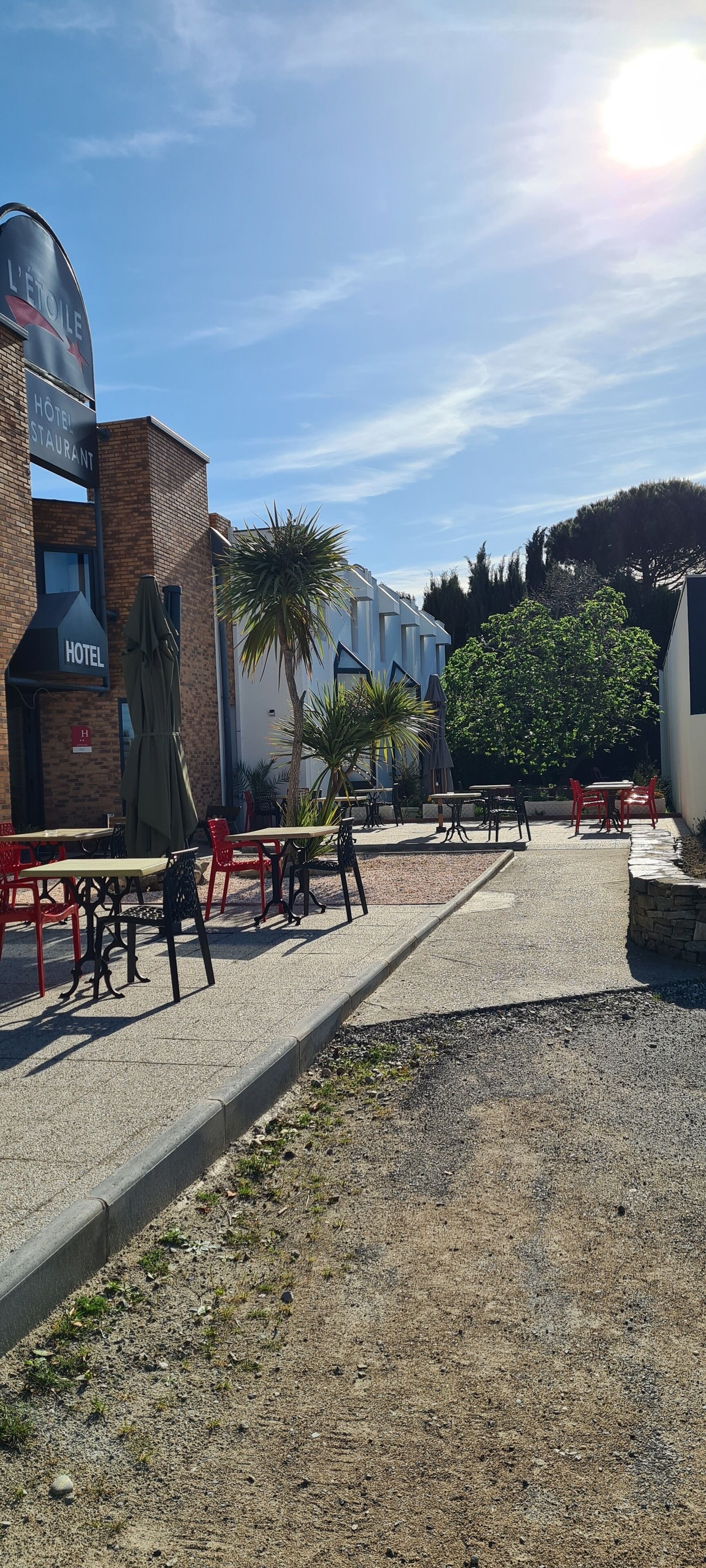 An outdoor patio area with tables and chairs, a brick building with a sign reading "HOTEL RESTAURANT," and a palm tree.