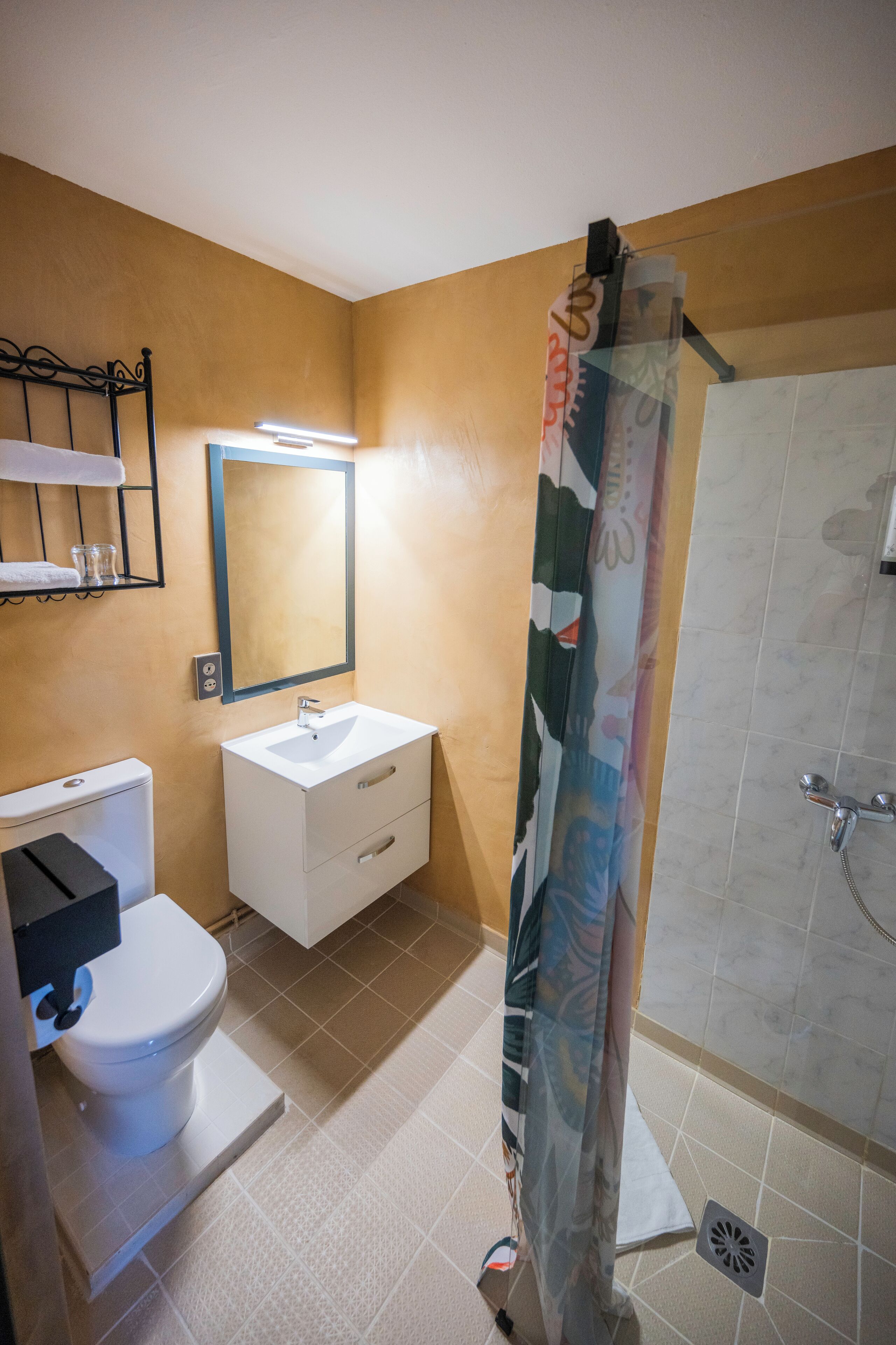 Un baño con inodoro, lavabo, espejo, ducha y suelo de baldosas.