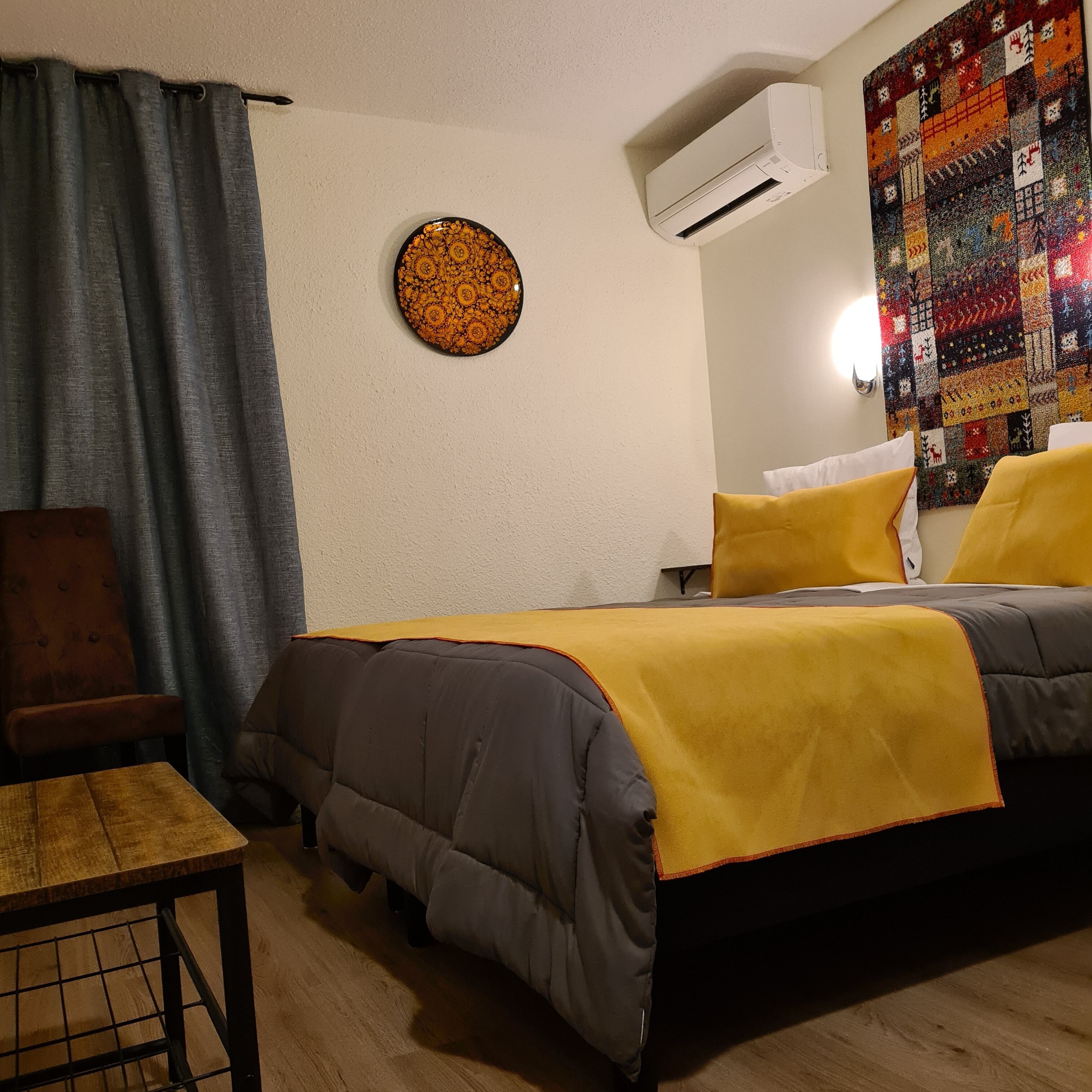 Un dormitorio con cama, una silla, un equipo de aire acondicionado y un adorno en la pared.