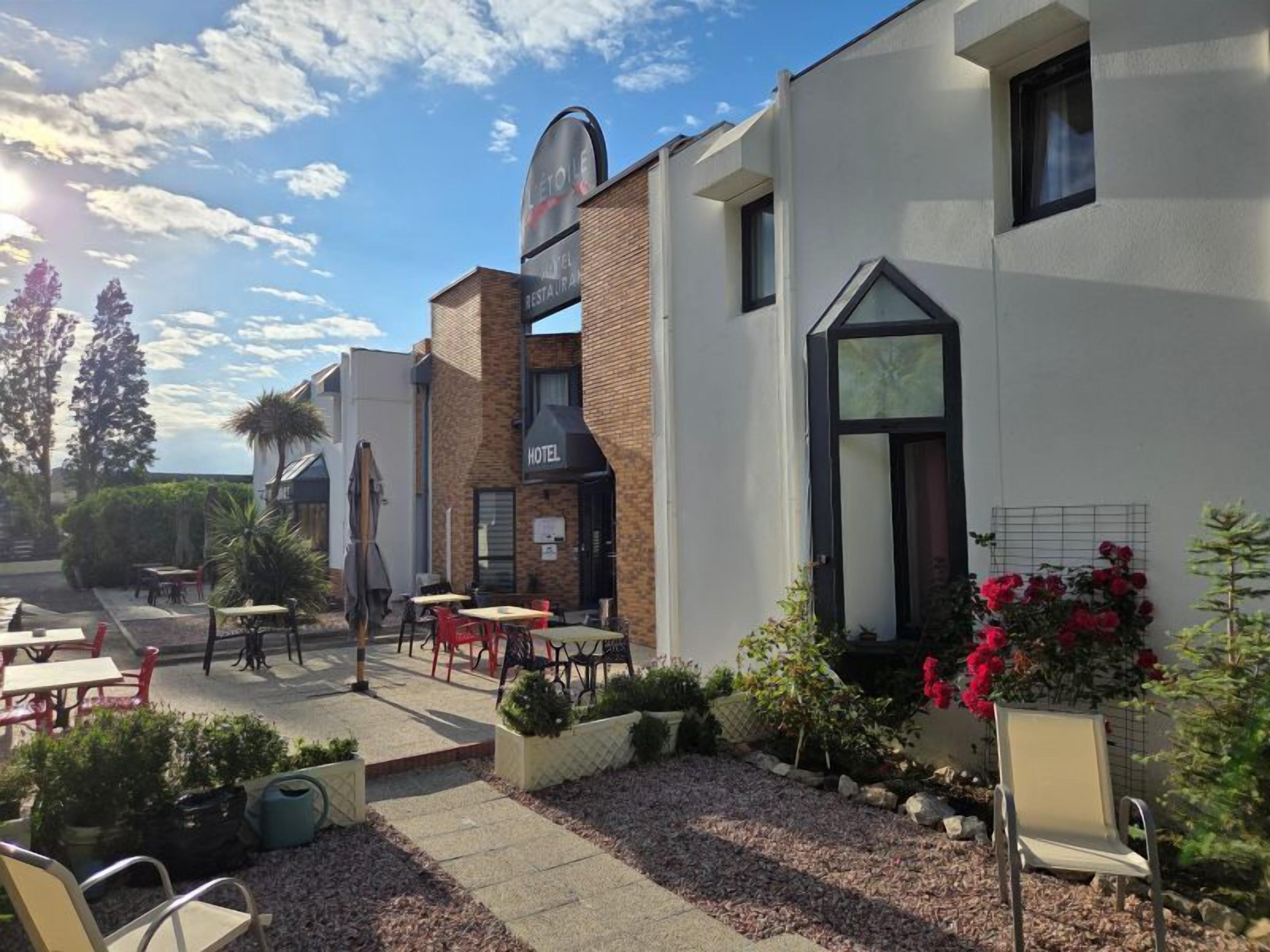 Un hotel con terraza al aire libre, fachada de ladrillo y jardín con plantas y flores.
