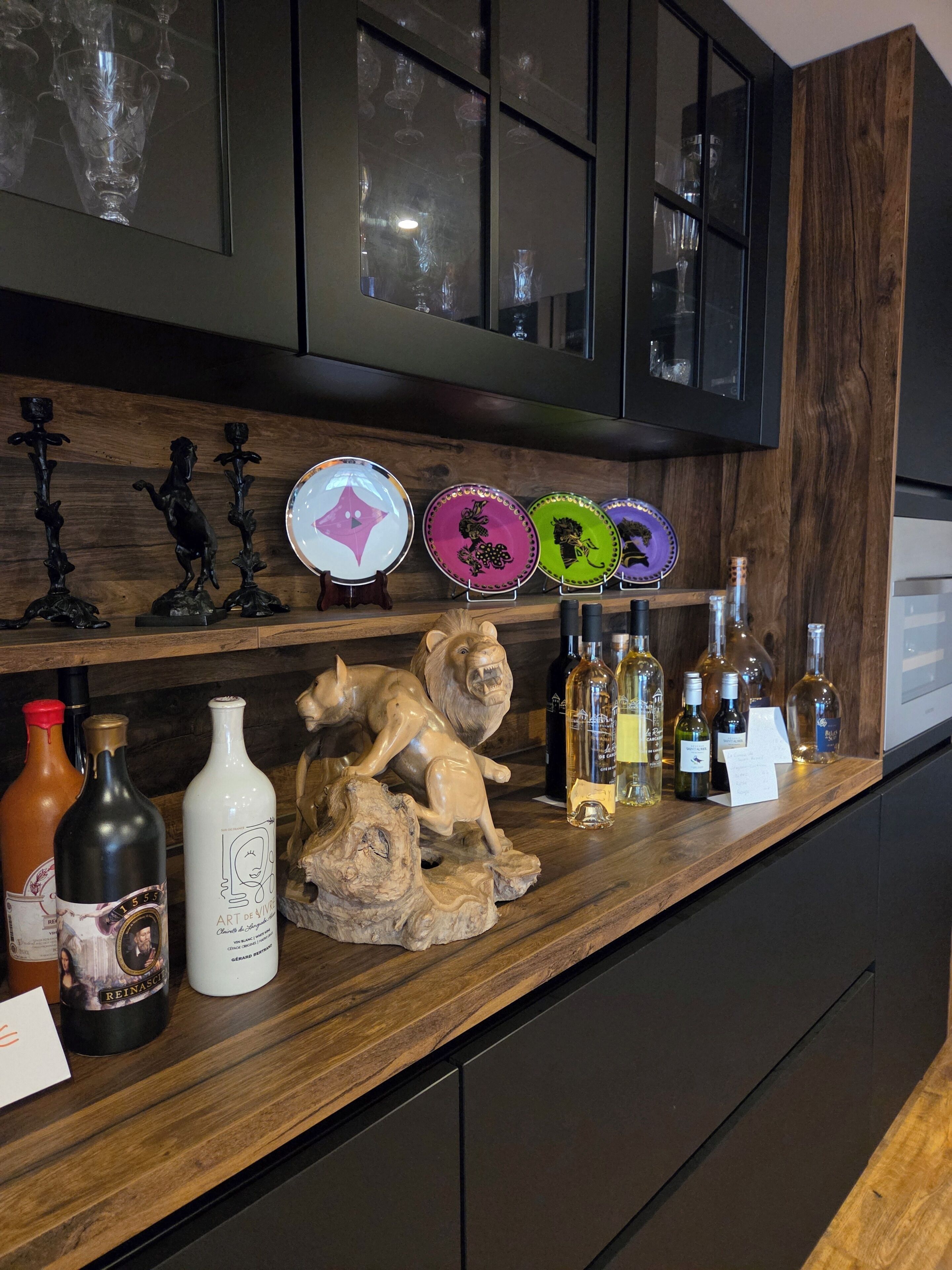 A bar area with a wooden countertop, wine bottles, decorative plates, and a lion sculpture.