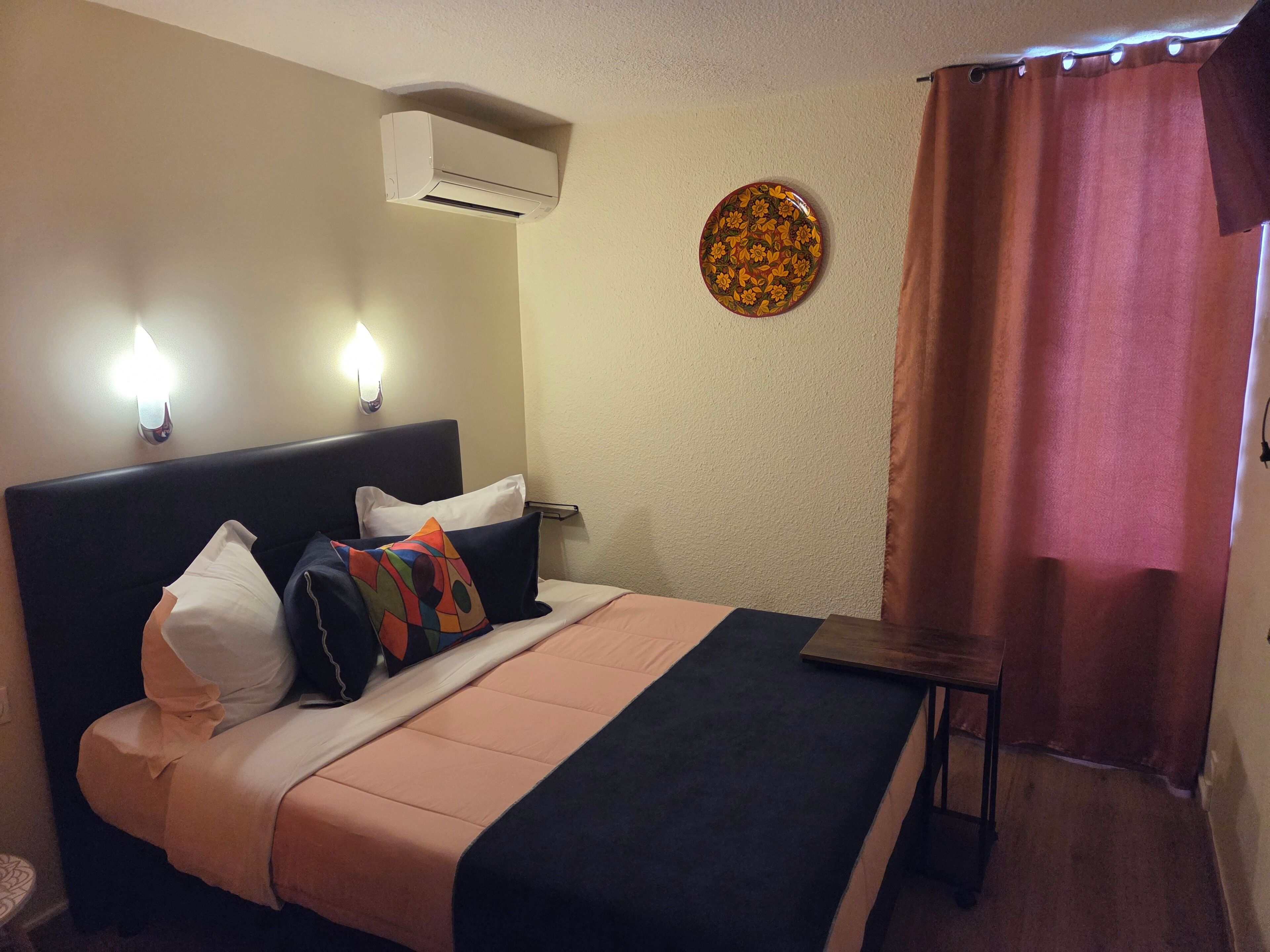Habitación de hotel con cama, equipo de aire acondicionado, luz de pared, plato decorativo y cortina.