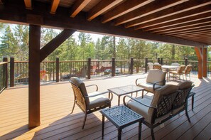A covered outdoor deck with wooden flooring, metal railings, and outdoor furniture including chairs and tables. - Bare Necessities (Big Bear Lake)