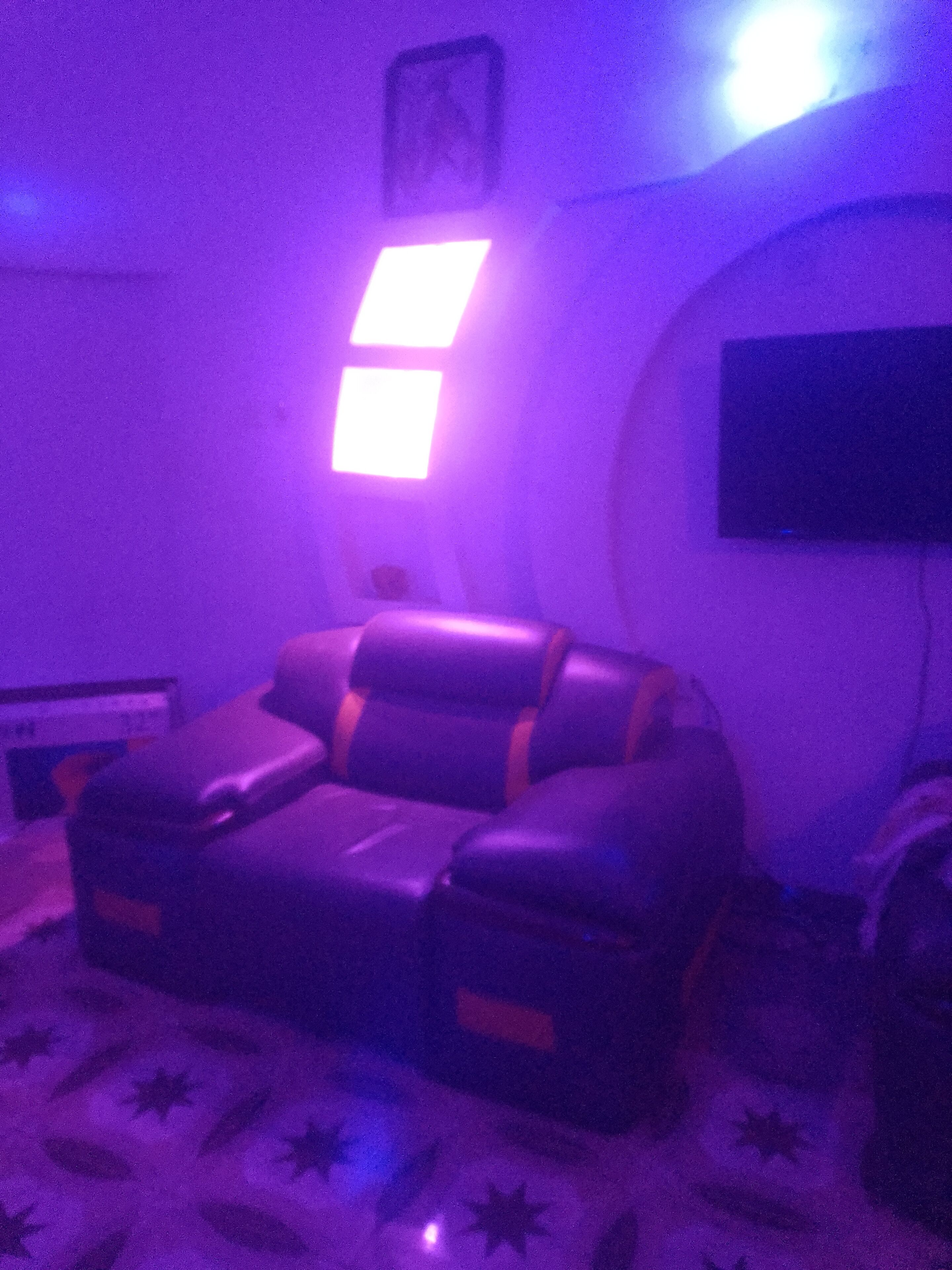 A room with a leather sofa, a flat-screen TV mounted on the wall, and a patterned rug.