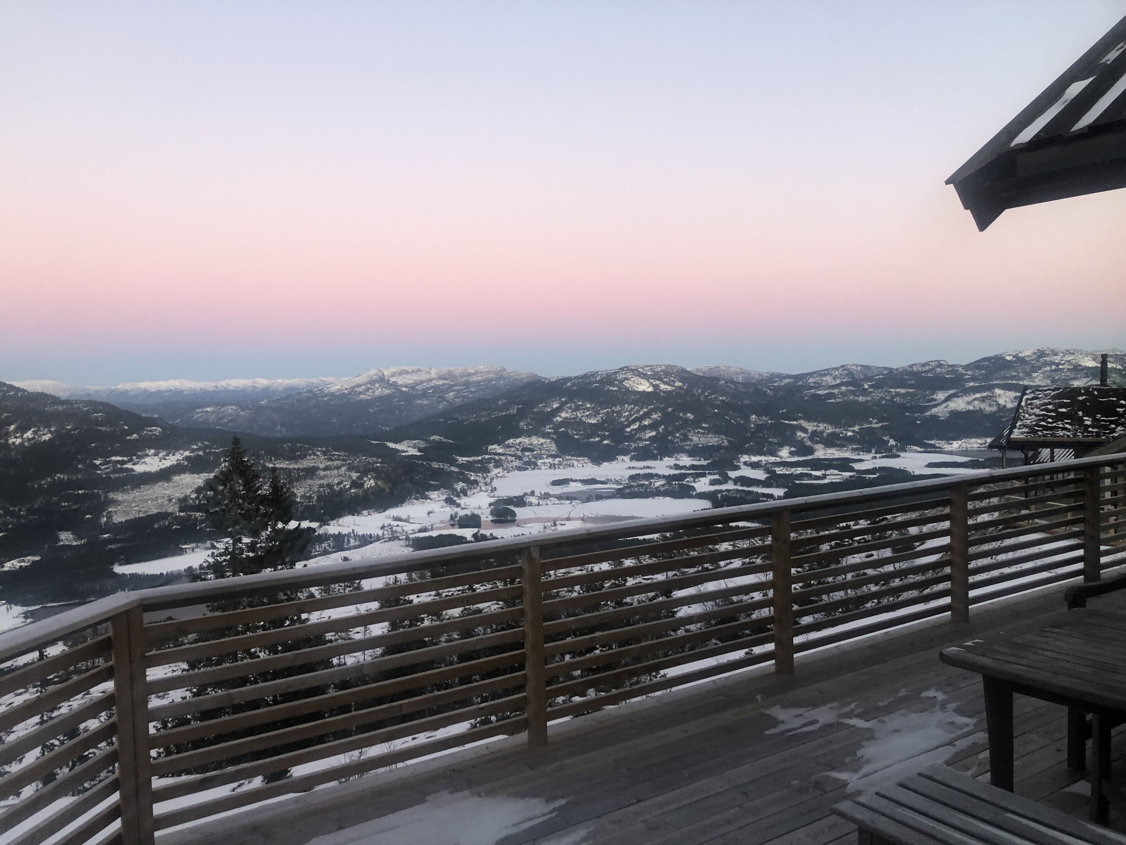 A wooden deck with a railing overlooking a snow-covered mountainous landscape.