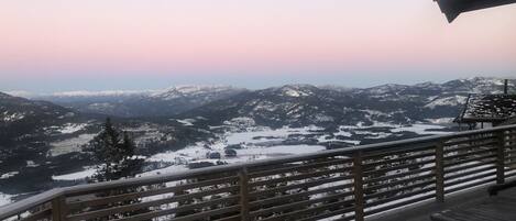 A wooden deck with a railing overlooking a snow-covered mountainous landscape.