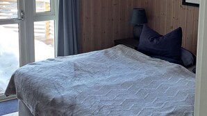 Et soveværelse med seng, trævægge, loftlampe, et vindue med gardiner og et billede i ramme på væggen.