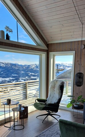 A modern room with large windows, a green chair, a small table, and a potted plant. - Dalblikken House: Vacation home for 8 people with 4 bedrooms (Vrådal)