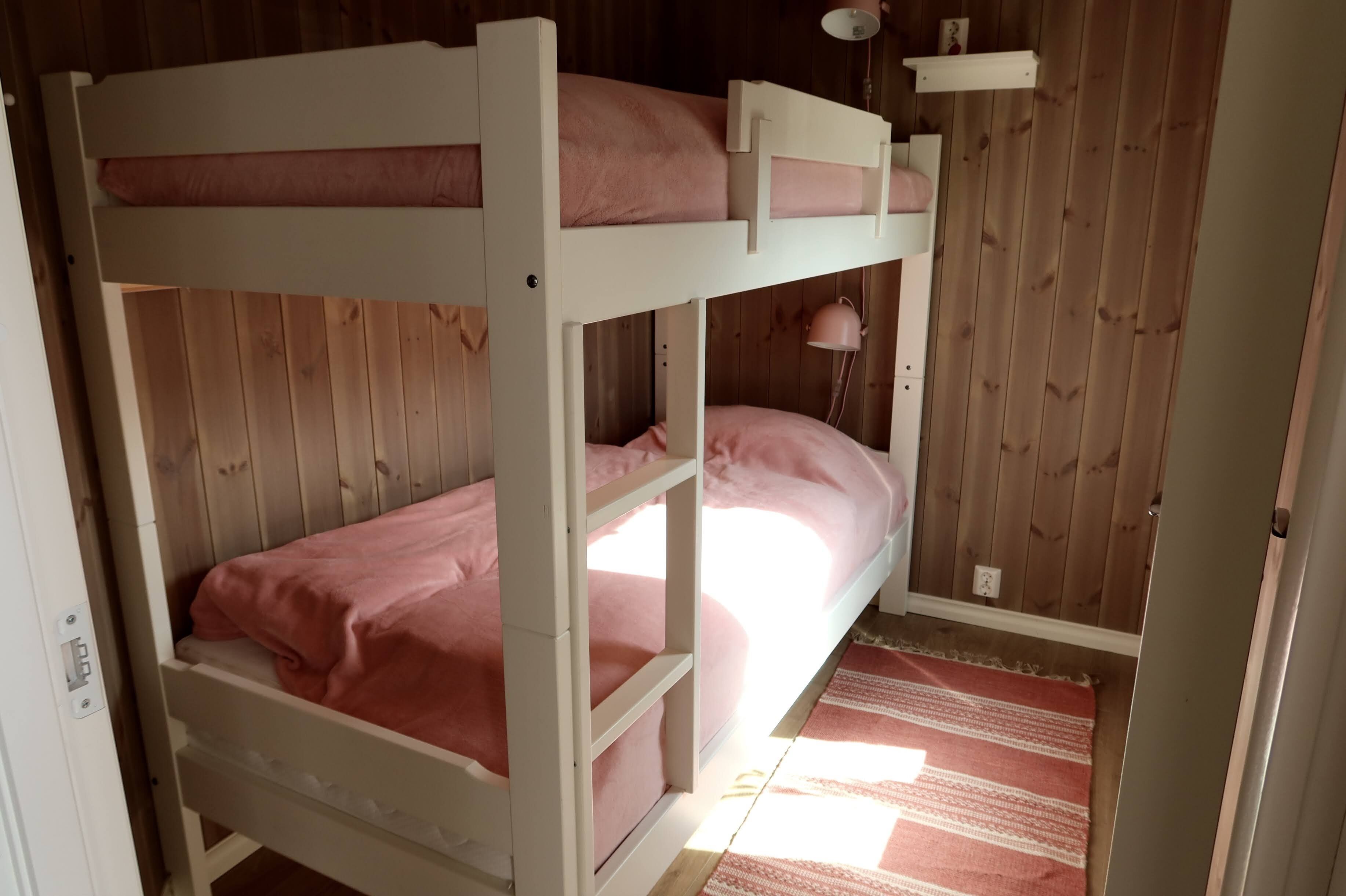 A bunk bed room with a wooden floor and a striped rug.