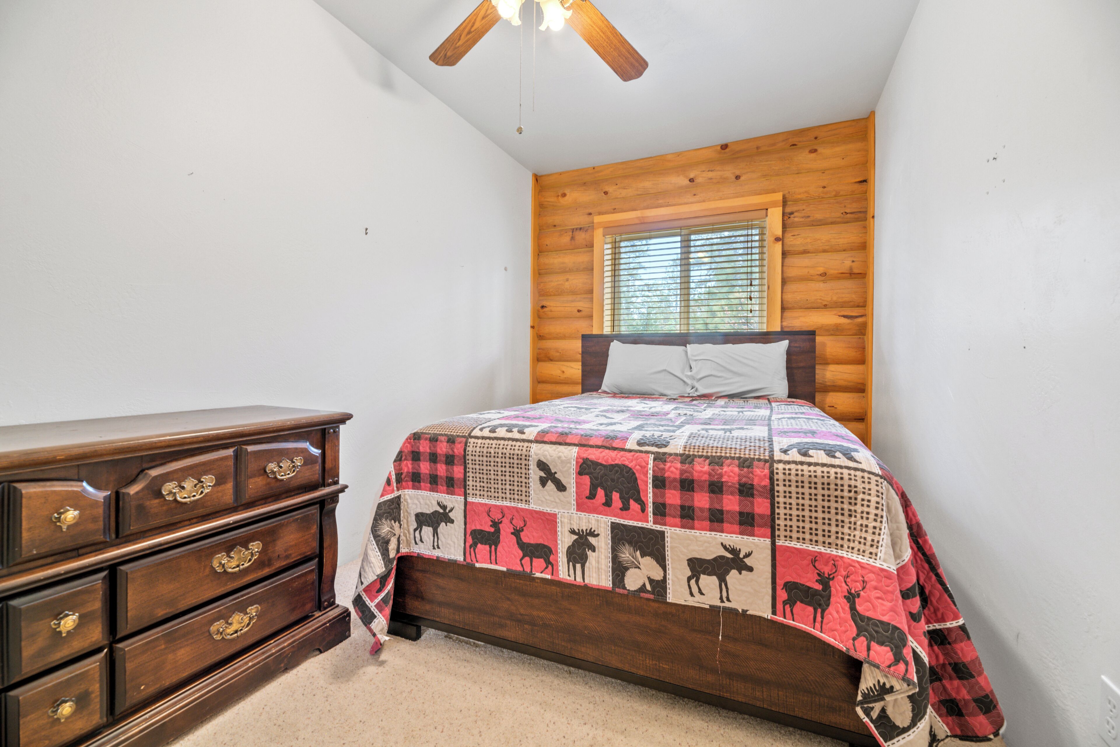 Un dormitorio con cabecera de madera, colcha con estampados de animales, cómoda de madera y ventana con persianas.
