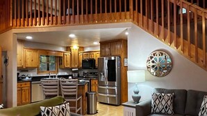 A spacious living area with a kitchen, wooden staircase, and modern furnishings.