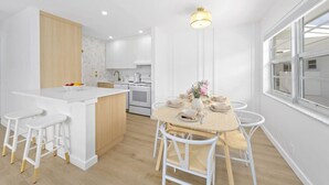 Una cocina moderna con armarios blancos, una isla central y un comedor con una mesa de madera y sillas blancas.