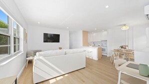 Un espacio habitable moderno y de planta abierta con un sofá blanco, una mesa de comedor y una cocina al fondo.