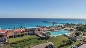 Un resort con piscina, un muelle que se adentra en el océano y un edificio grande con techo rojo.