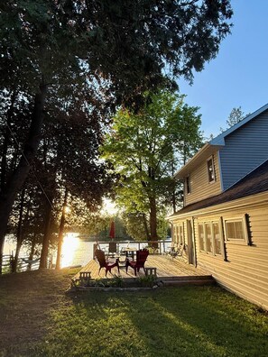 A wooden deck with outdoor furniture, a view of a lake, and a two-story building with windows.