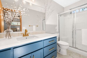Ein modernes Badezimmer mit einer Duschkabine aus Glas, einer weißen Toilette und einem Waschtisch mit blauen Schränken und einem goldenen Wasserhahn.