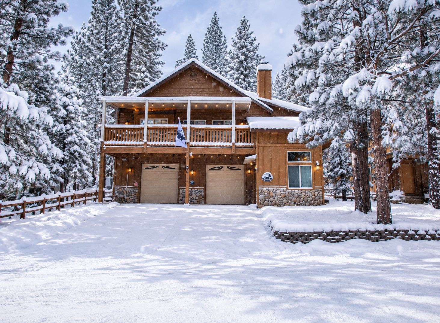 A two-story log cabin with a balcony, stone foundation, and a garage.