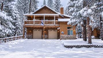A two-story log cabin with a balcony, stone foundation, and a garage.