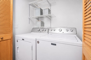 Un área de lavandería con dos lavadoras y secadoras Maytag, un estante metálico sobre las secadoras y una puerta de madera con manija.