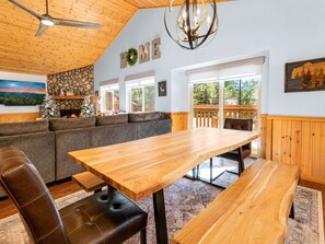 Un interior acogedor con techo de madera, chimenea de piedra, una amplia mesa de comedor de madera y un espacio de descanso confortable.
