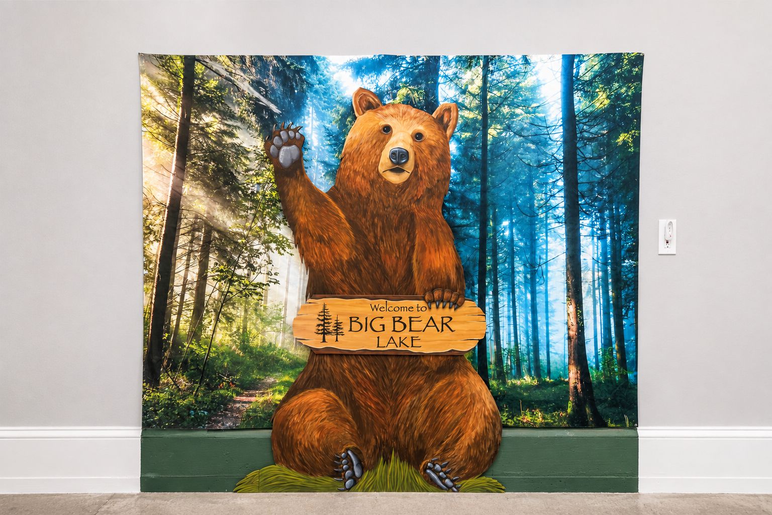 A bear holding a sign that reads 'Welcome to Big Bear Lake' in a forest setting.