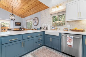Una cocina moderna con armarios azules, techo de madera y lavavajillas de acero inoxidable.