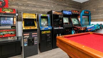 A pool table with arcade machines in a room with wooden walls.