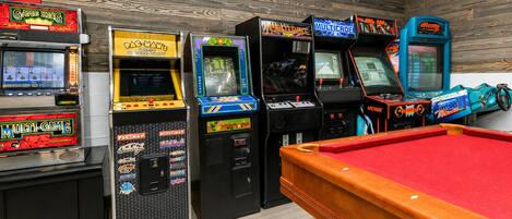 A pool table with arcade machines in a room with wooden walls.