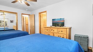 Un dormitorio con dos camas, muebles de madera, un cuadro y un ventilador de techo.
