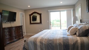 A bedroom with a large bed, a dresser, a television mounted on the wall, and a sliding glass door leading to a balcony.