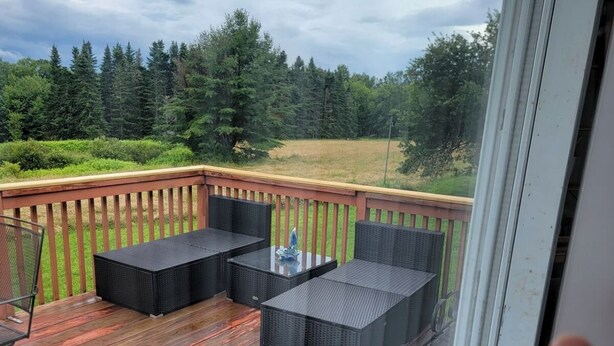 A deck with outdoor furniture, a glass table, and a view of a forest.