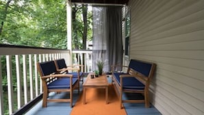 A covered porch with two wooden chairs and a table, surrounded by a white railing and a view of greenery. - Open 4BR Near Downtown Boston Backyard, Fire Pit, Grills & Walk to Train (Boston)