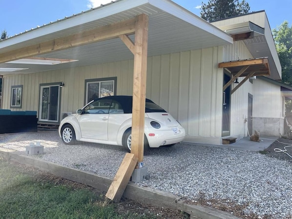 Une voiture blanche est garée sous une zone abritée, dont la structure est faite de poutres en bois.